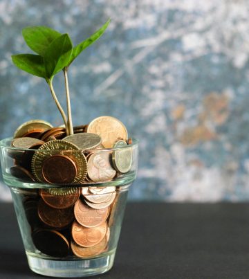 A glass with coins and a small plant in it.